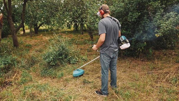 Cortador de grama profissional cortando grama verde no pomar usando cortador de cordas
. - Foto, Imagem