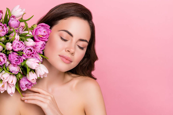 Photo of shiny charming woman naked shoulders holding flowers closed eyes empty space isolated pink color background. - Zdjęcie, obraz