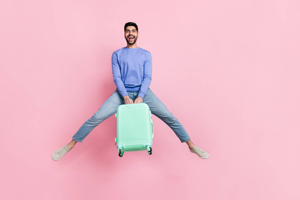 Full length photo of cute impressed arab guy dressed blue pullover jumping high holding bag empty space isolated pink color background. - Φωτογραφία, εικόνα