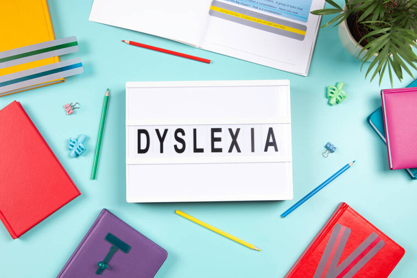 Dyslexia awareness, help children with reading, learning difficulties concept. Lightbox with DYSLEXIA word, colorful books and open book with reading highlight bookmark overlays strips. Top view. - Фото, изображение
