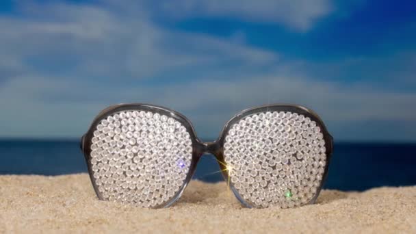 Pari kristallin peittämiä kuohuvia aurinkolaseja rannalla ohimenevillä pilvillä  - Materiaali, video