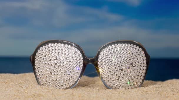 Une paire de lunettes de soleil étincelantes recouvertes de cristal sur la plage avec des nuages qui passent  - Séquence, vidéo