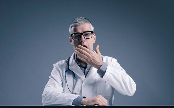 Sleepy overworked doctor yawning and covering his mouth with his hand - Foto, afbeelding