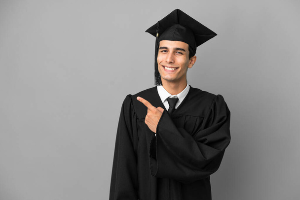 Young Argentinian university graduate isolated on grey background pointing to the side to present a product - Foto, imagen