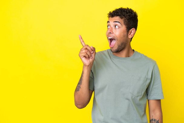 Молодий вродливий бразильський чоловік, ізольований на жовтому фоні, має намір зрозуміти рішення, підносячи вгору палець. - Фото, зображення