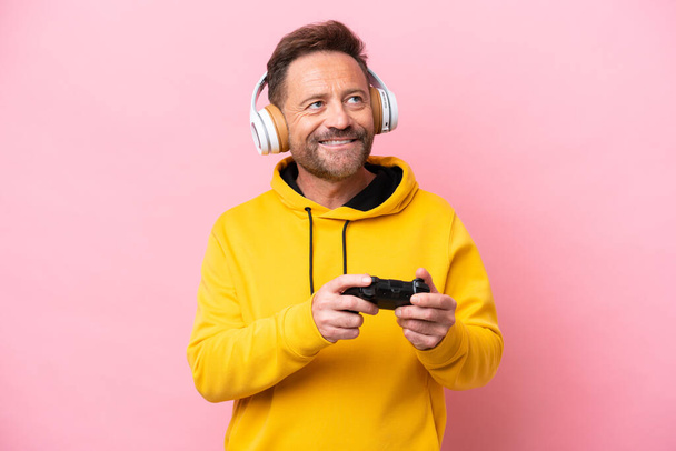 Hombre de mediana edad jugando con un controlador de videojuegos aislado sobre fondo rosa pensando en una idea mientras mira hacia arriba - Foto, Imagen