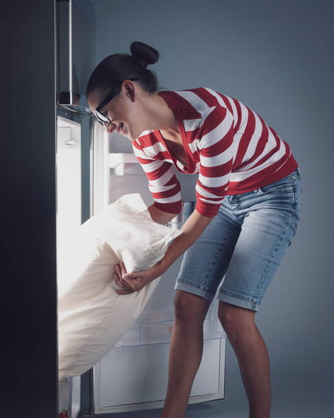 Happy woman putting her bed pillow in the fridge, hot weather and heatwave concept - Foto, Imagem