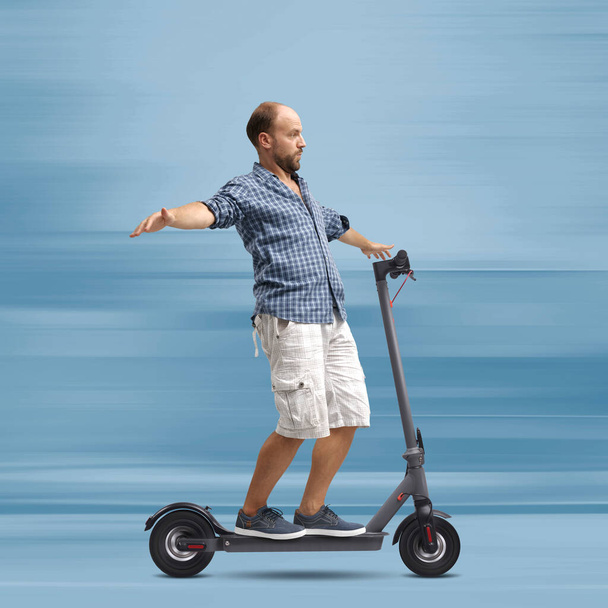 Elektrikli scooter kullanan dikkatsiz bir adam elleri boşta, kolları açık balya yapıyor. - Fotoğraf, Görsel