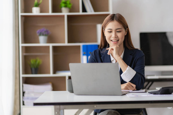 Adorable Asian businesswoman enjoying success working in the office with her laptop and company financial accounting documents. - Photo, Image