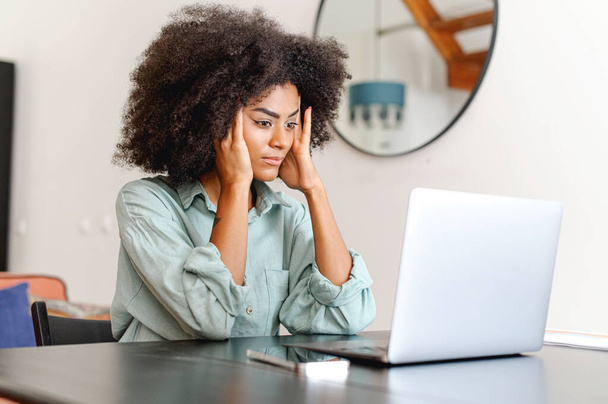 Confused black woman looking at laptop screen in despair, unemployed female looking through job hunting sites unsuccessfully, frustrated female freelancer fails - Fotografie, Obrázek