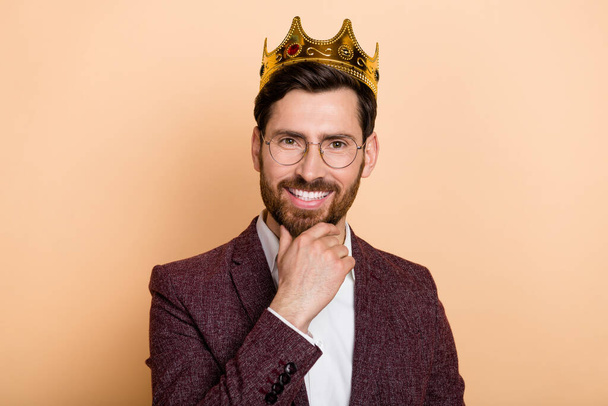 Portrait of young good looking groomed gentleman with golden crown brainstorming isolated on beige color background. - Foto, Imagen