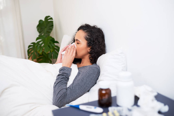 A young multi-ethnic woman blows her nose while recovering from flu in bed. High quality photo - Photo, Image