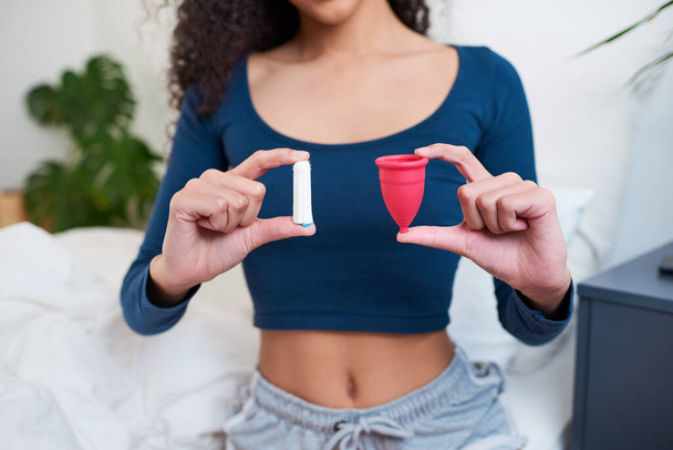 Foto recortada de mujer joven sosteniendo tampón y copa menstrual como comparación. Foto de alta calidad - Foto, imagen