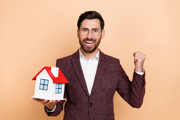 Foto de loco agente de bienes raíces alegres celebrar su logro vender casa aislada sobre fondo de color beige. - Foto, Imagen