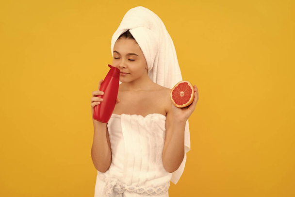 glückliches Kind im Handtuch riecht Grapefruit Shampoo-Flasche auf gelbem Hintergrund. - Foto, Bild