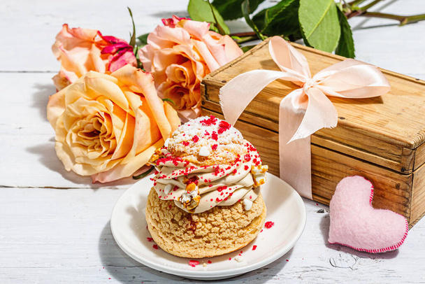 Het concept van een romantisch geschenk. French Shu cake, hibiscus thee, boeket rozen, feestelijk decor. Valentijnsdag concept, Vrouwendag 8 maart, Bruiloft. Witte planken, achtergrond, close up - Foto, afbeelding