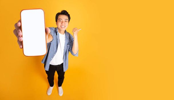 изображение азиатского человека, держащего телефон, изолированный на желтом фоне - Фото, изображение