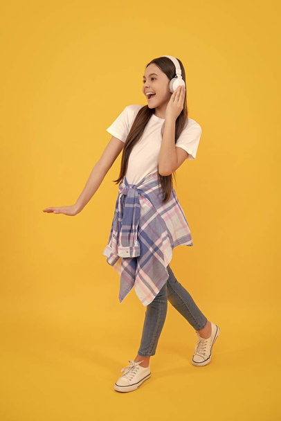 Happy teen girl in headphones singing along to song yellow background, music. - Foto, Imagen