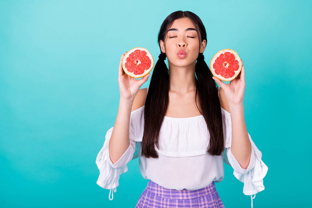 Photo of positive dreamy lady wear white holding two orange halves sending kiss empty space isolated turquoise color background. - Foto, imagen