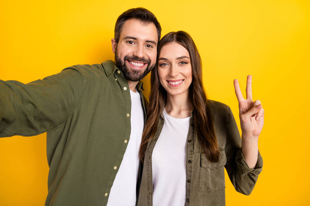 Self-portrait of attractive cheerful couple bonding showing v-sign good mood isolated over bright yellow color background. - Foto, immagini