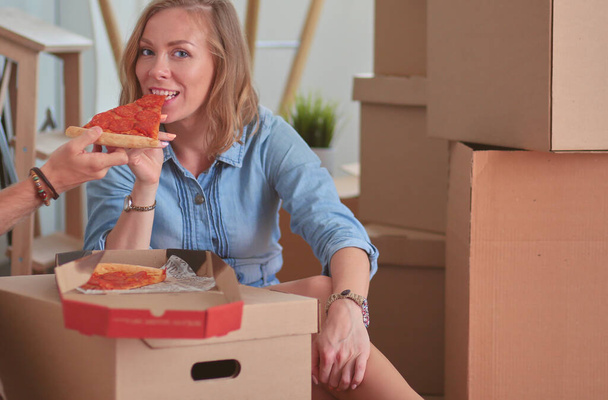 Young couple have a pizza lunch break on the floor after moving into a new home with boxes around them. Young couple. - Foto, imagen