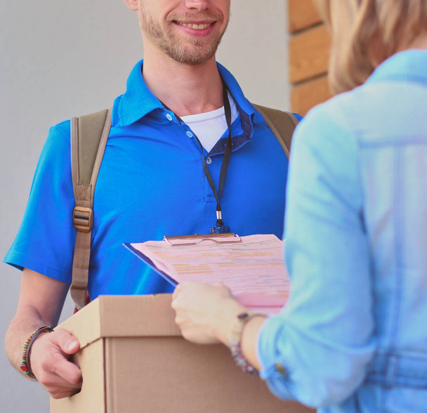 Smiling delivery man in blue uniform delivering parcel box to recipient - courier service concept. Smiling delivery man in blue uniform. - Fotografie, Obrázek