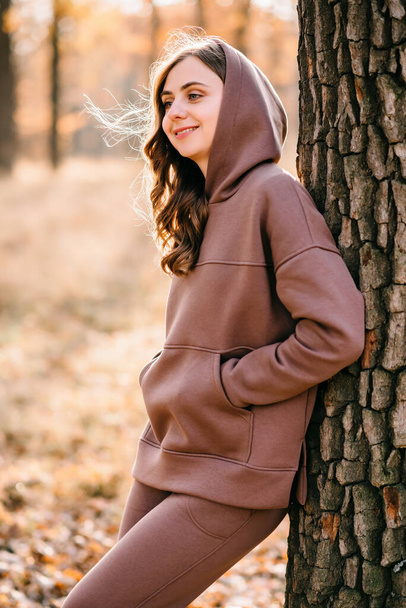 Jovem mulher de camisola com capuz sorrindo em um parque de outono. Tempo ensolarado. Temporada de outono. - Foto, Imagem