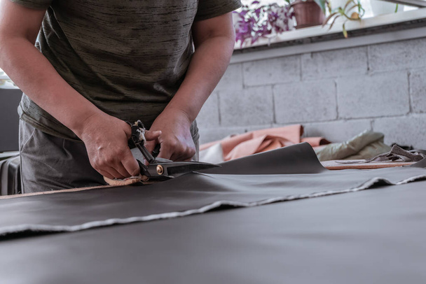 A cutter cuts fabric with scissors in a sewing workshop - Фото, изображение