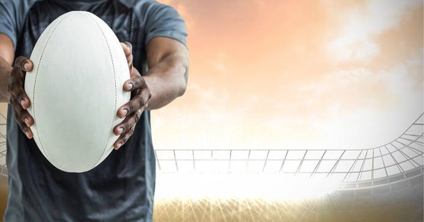 Composition of male rugby player holding rugby ball over sports stadium. sport and competition concept digitally generated image. - 写真・画像