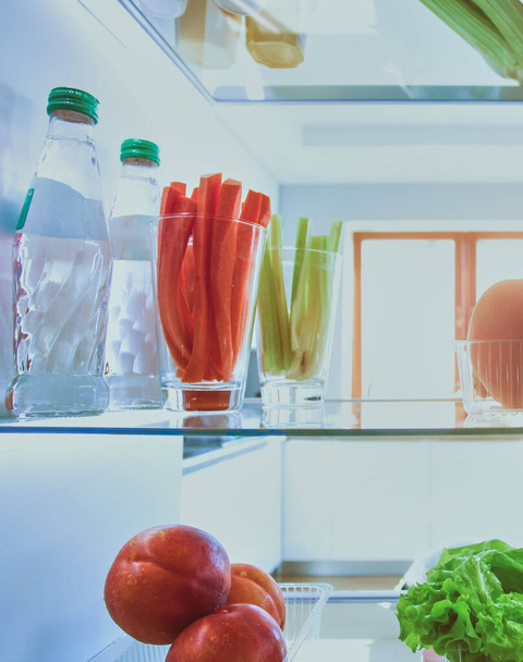 Portret van een vrouw in de buurt van een open koelkast vol gezond voedsel, groenten en fruit. Portret van een vrouw. - Foto, afbeelding