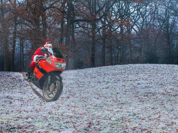 Kerstavond. De kerstman op een rode motorfiets rijdt snel door het winterbos. Het concept van een gezonde en moderne levensstijl. Plaats voor tekst. - Foto, afbeelding