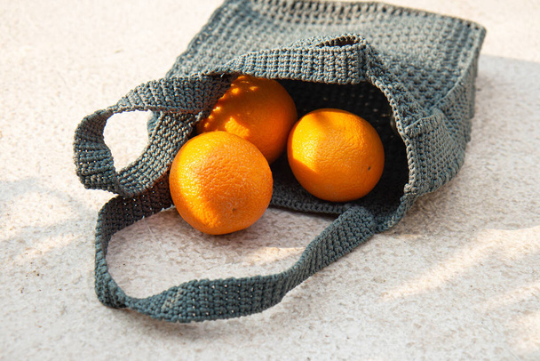 Grey knitted bag handmade and ripe oranges outdoors. Sustainable shopping. Waste-fr ee lifestyle. Do-it-yourself jute bag - Photo, image