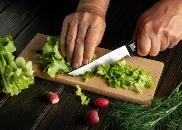 El chef prepara ensalada de lechuga y rábano en casa cortando con un cuchillo. Cocina vegetariana o comida - Foto, imagen