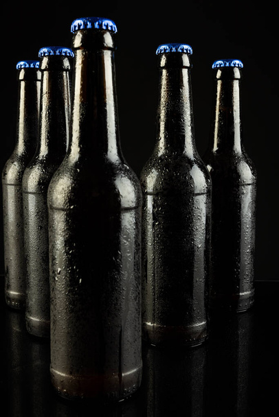 Image of five beer bottles with blue crown caps, with copy space on black background. Drinking alcohol, refreshment and lager day celebration concept. - Foto, afbeelding