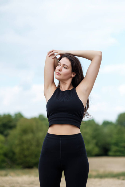 Młoda biała kobieta uprawia jogę i rozciąga się w lesie w Londynie. Ma na sobie czarny strój do jogi... - Zdjęcie, obraz