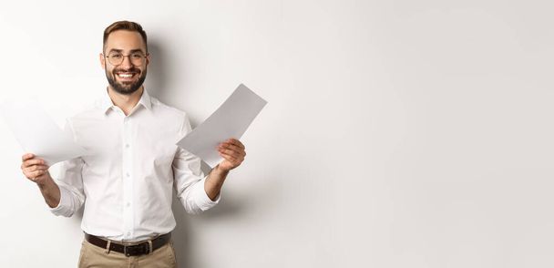 Satisfied boss smiling while holding good report, reading documents, standing over white background. - Photo, Image