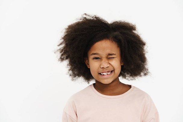 Black preteen girl with curly hair smiling and winking at camera isolated over white background - Fotoğraf, Görsel