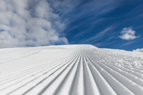 Close-up straight line rows of freshly prepared groomed ski slope piste with bright shining sun and clear blue sky background. Snowcapped mountain downhill landscape at europe winter skiing resort. - Photo, Image