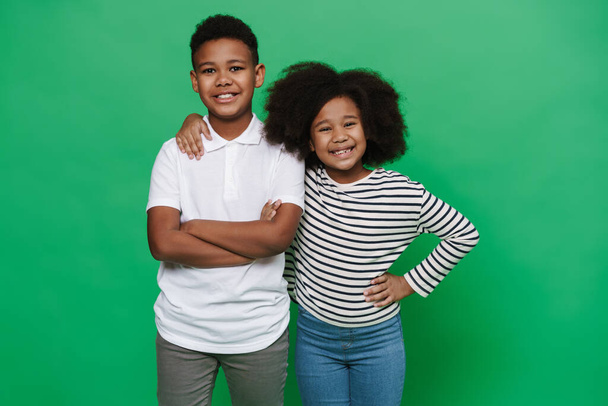 Black boy and girl smiling and hugging together at camera isolated over green background - Φωτογραφία, εικόνα