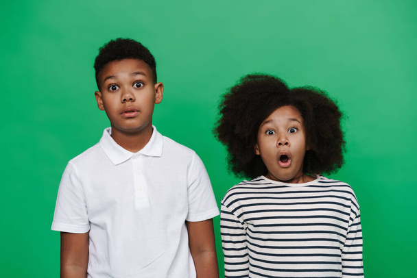Black boy and girl expressing surprise together at camera isolated over green background - Fotografie, Obrázek