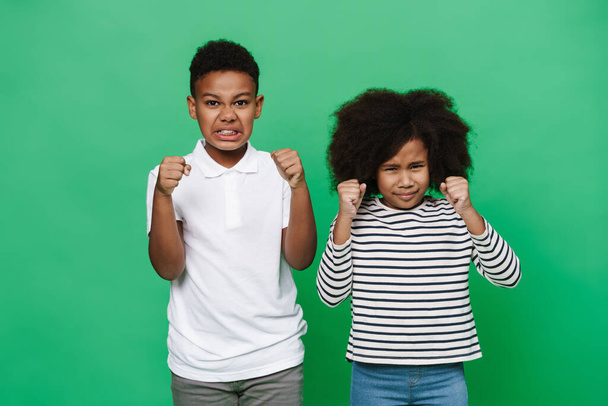 Black boy and girl posing with clenched fists together isolated over green background - Fotoğraf, Görsel