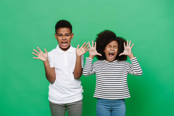 Black boy and girl screaming while showing their palms together isolated over green background - Foto, Bild