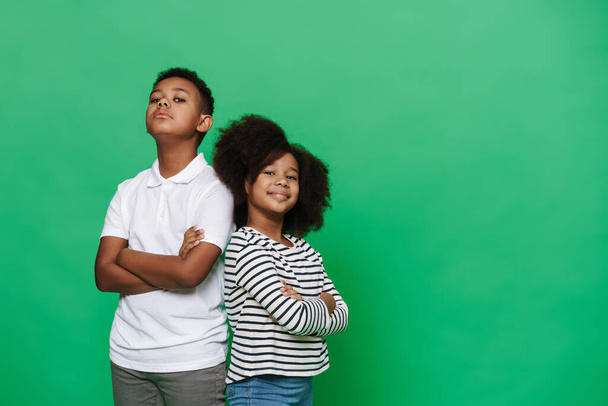 Black boy and girl smiling while posing with arms crossed isolated over green background - Fotó, kép