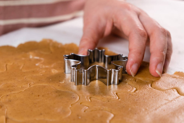 Close up woman hands cutting out cookies with metal mold from the shortcrust pastry. A metal forms in the form of snowflakes for making gingerbread for Christmas. - Foto, afbeelding