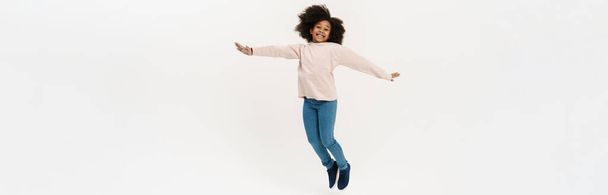 Black preteen girl with curly hair jumping and laughing isolated over white background - Photo, image
