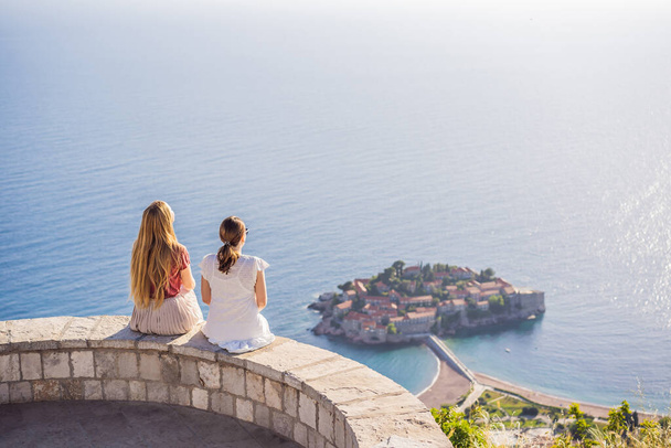 Two Woman tourist on background of beautiful view of the island of St. Stephen, Sveti Stefan on the Budva Riviera, Budva, Montenegro. Travel to Montenegro concept. - Foto, imagen
