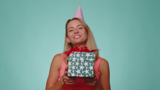 Pozytywnie uśmiechnięta blondynka prezentująca pudełko prezentów urodzinowych wyciąga ręce, oferuje zapakowany prezent premii kariery, świętując imprezę. młody dorosły dziewczyna odizolowany sam na niebieski studio ściany tle - Materiał filmowy, wideo