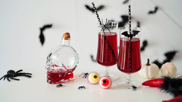 Close-up van twee bloederige cocktails glazen bekers voor Halloween, fles vorm schedel, snoep ogen, vleermuizen, spinnen, pompoenen witte achtergrond.Decor concept voor Halloween feest, alcoholische dranken, cranberry punch. - Foto, afbeelding