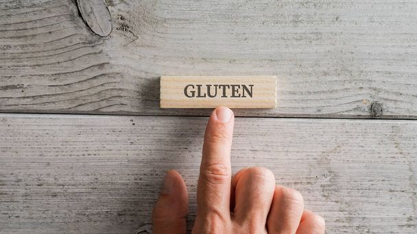 Male hand placing wooden peg with a Gluten sign on it over white textured wooden background. - Фото, зображення