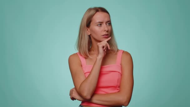 Need to think. Doubting pensive blonde woman pondering and imagining in mind, wondering difficult solution, feeling confused, not sure about choice. Young girl isolated on blue studio background - Footage, Video